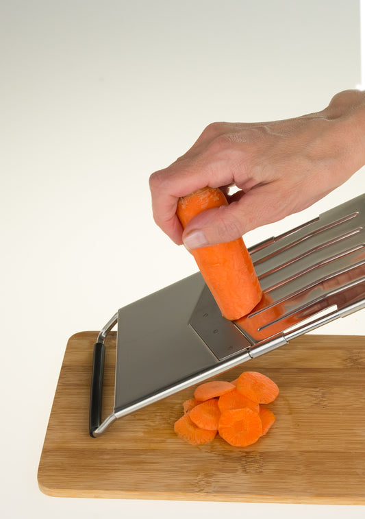 Mandolina in acciaio inox Ideale Ipac utilizzata su un tagliere in legno per affettare carote a rondelle uniformi
