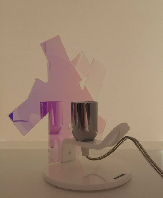 Lampada da tavolo in metacrilato dalla colorazione particolare flash (effetto specchio iridescente). Base e supporto in metacrilato bianco e portalampadina in metallo cromato. Si può applicare qualsiasi lampadina con attacco filettato E 27 (non inclusa). Dimensioni: cm 23 x 23 x 15 p. In negozio e online su tuttochic.it