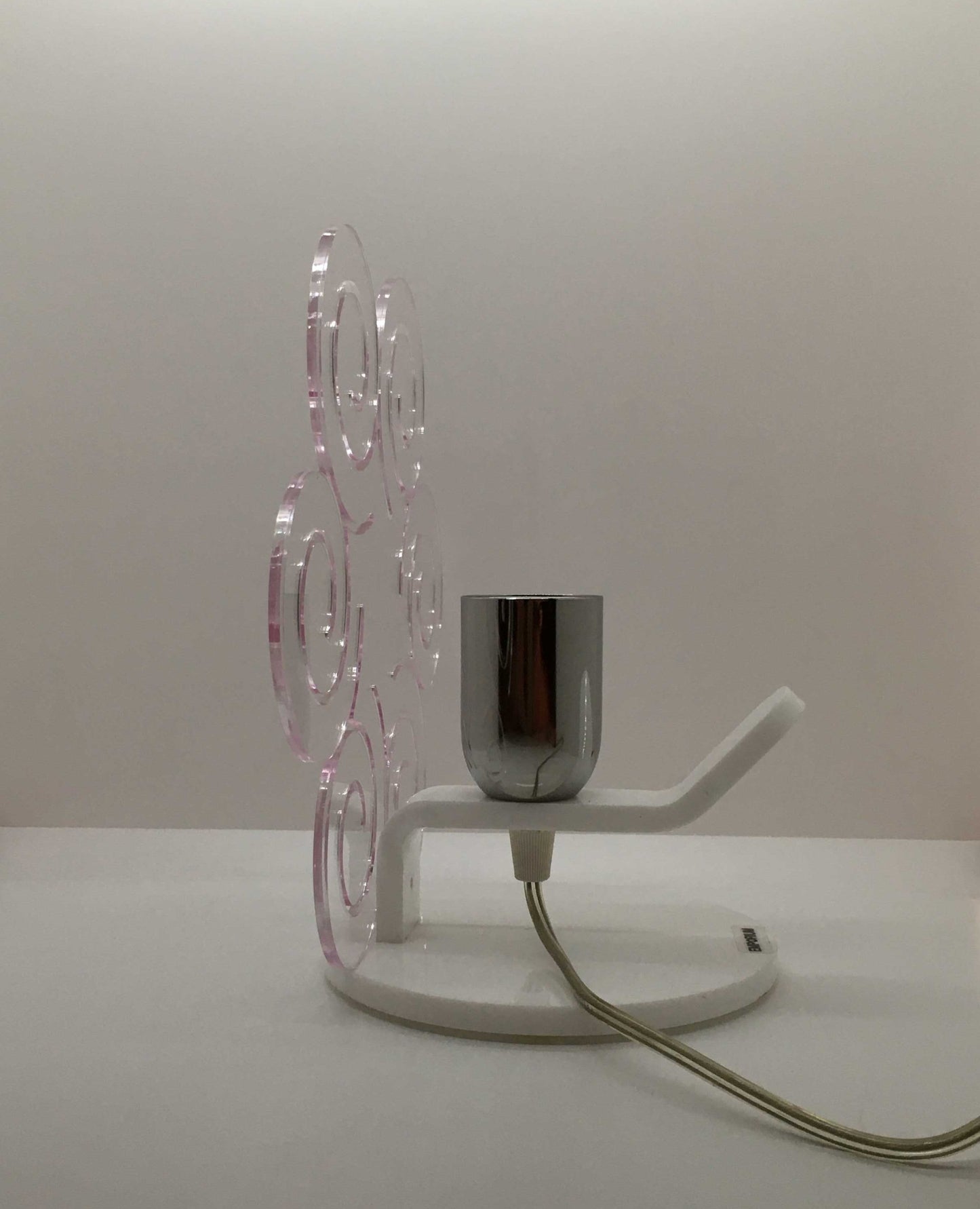 Lampada da tavolo in metacrilato trasparente con profilo viola soft. Base e supporto in metacrilato bianco e portalampadina in metallo cromato. Si può applicare qualsiasi lampadina con attacco filettato E 27 (non inclusa). Dimensioni: cm 23 x 23 x 15 p. In negozio e online su tuttochic.it