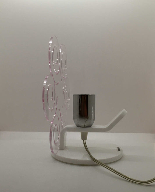 Lampada da tavolo in metacrilato trasparente con profilo viola soft. Base e supporto in metacrilato bianco e portalampadina in metallo cromato. Si può applicare qualsiasi lampadina con attacco filettato E 27 (non inclusa). Dimensioni: cm 23 x 23 x 15 p. In negozio e online su tuttochic.it