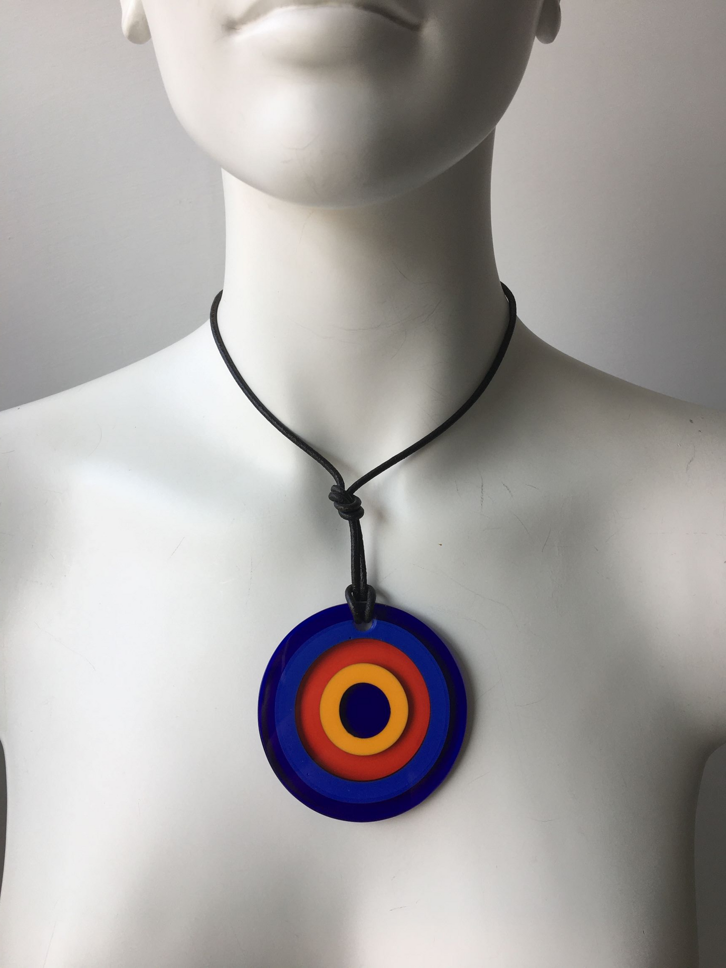 Pendente in cristallo di Murano rifinito a mano con motivi decorativi applicati a caldo: murrina ad anelli. Dotato di laccetto in cuoio. Dimensioni: diametro cm 6,5