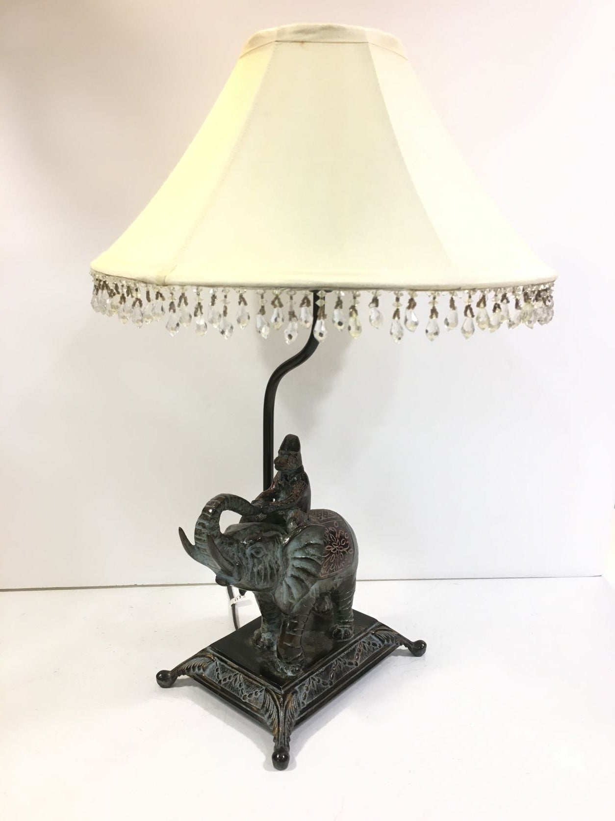 Lampada d'arredo in metallo effetto bronzo di colore verde con paralume in tessuto di colore beige chiaro decorato con strass in acrilico trasparente. Alimentazione: lampadina attacco E27 max 60 W Dimensioni: base cm. 21 x 16 x 55 H - paralume ø 35. In negozio e online su tuttochic.it