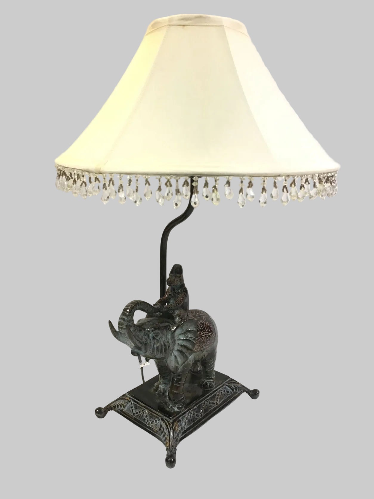 Lampada d'arredo in metallo effetto bronzo di colore verde con paralume in tessuto di colore beige chiaro decorato con strass in acrilico trasparente. Alimentazione: lampadina attacco E27 max 60 W Dimensioni: base cm. 21 x 16 x 55 H - paralume ø 35. In negozio e online su tuttochic.it
