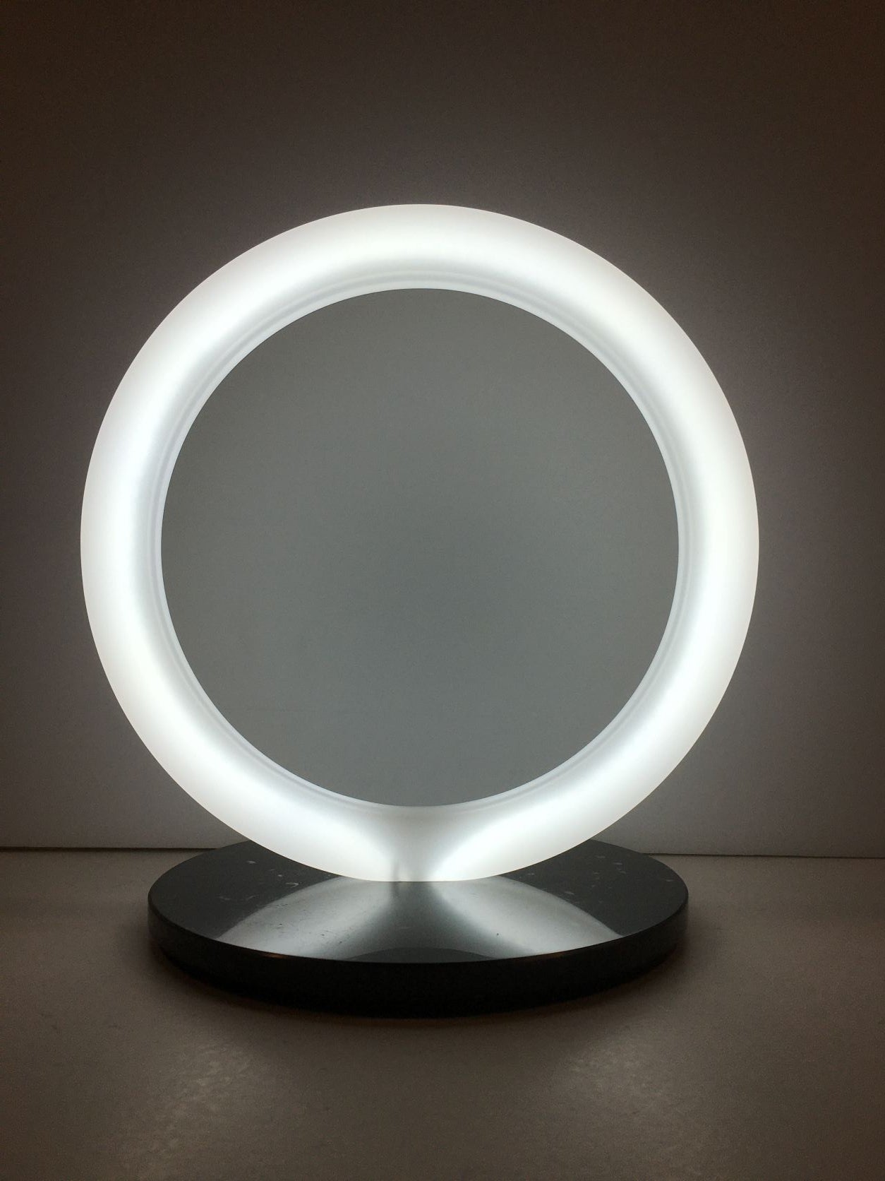 Lampada a forma di anello in cristallo acrilico opalino con base in marmo nero. Dimensioni cm 30 x 23 x 31,5 h. spessore 20 mm anello spessore 15 mm base Tipologia illuminazione led bianco freddo 24v – 8W / Mt Consumo 7W Grado luminosità 7000°K Lunghezza cavo 230 cm con interruttore. In negozio e online su tuttochic.it