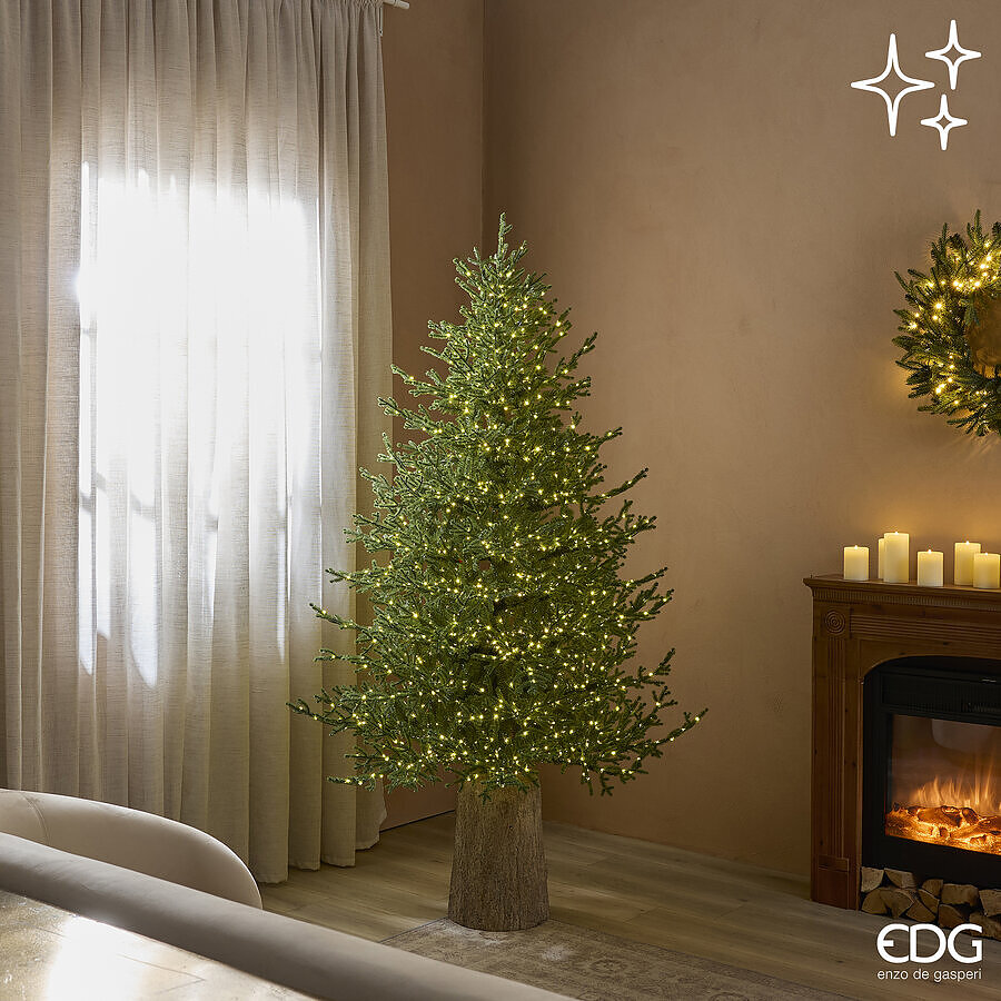 Elegante albero di Natale modello Pino Lucciole alto 180 cm di EDG Enzo De Gasperi acceso con 2300 luci LED calde in una stanza vicino a un camino.