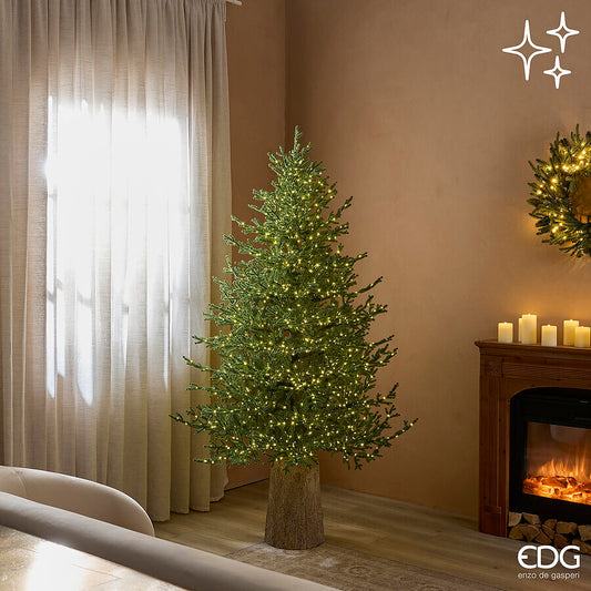 Elegante albero di Natale modello Pino Lucciole alto 180 cm di EDG Enzo De Gasperi acceso con 2300 luci LED calde in una stanza vicino a un camino.