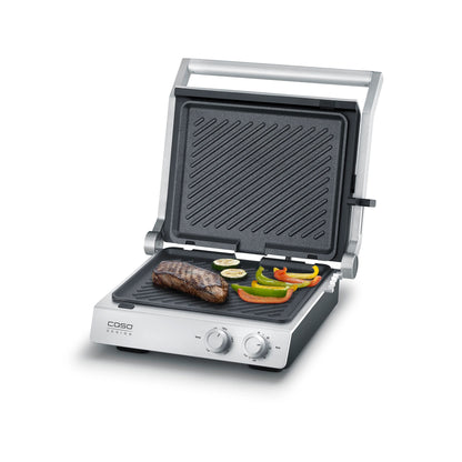 Piastra elettrica SteakChef CASO Design aperta su tavolo da cucina con bistecche in cottura