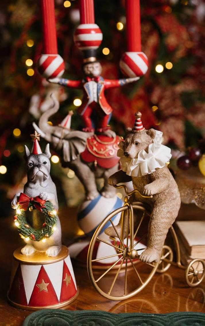 Statuina natalizia decorativa in resina a forma di orsetto marrone chiaro da circo con colletto bianco, mentre pedala su un antico biciclo vintage color oro lucido, altezza 25,5 cm, collezione Velvet Luxury Nuvole di Stoffa, Tutto Chic.