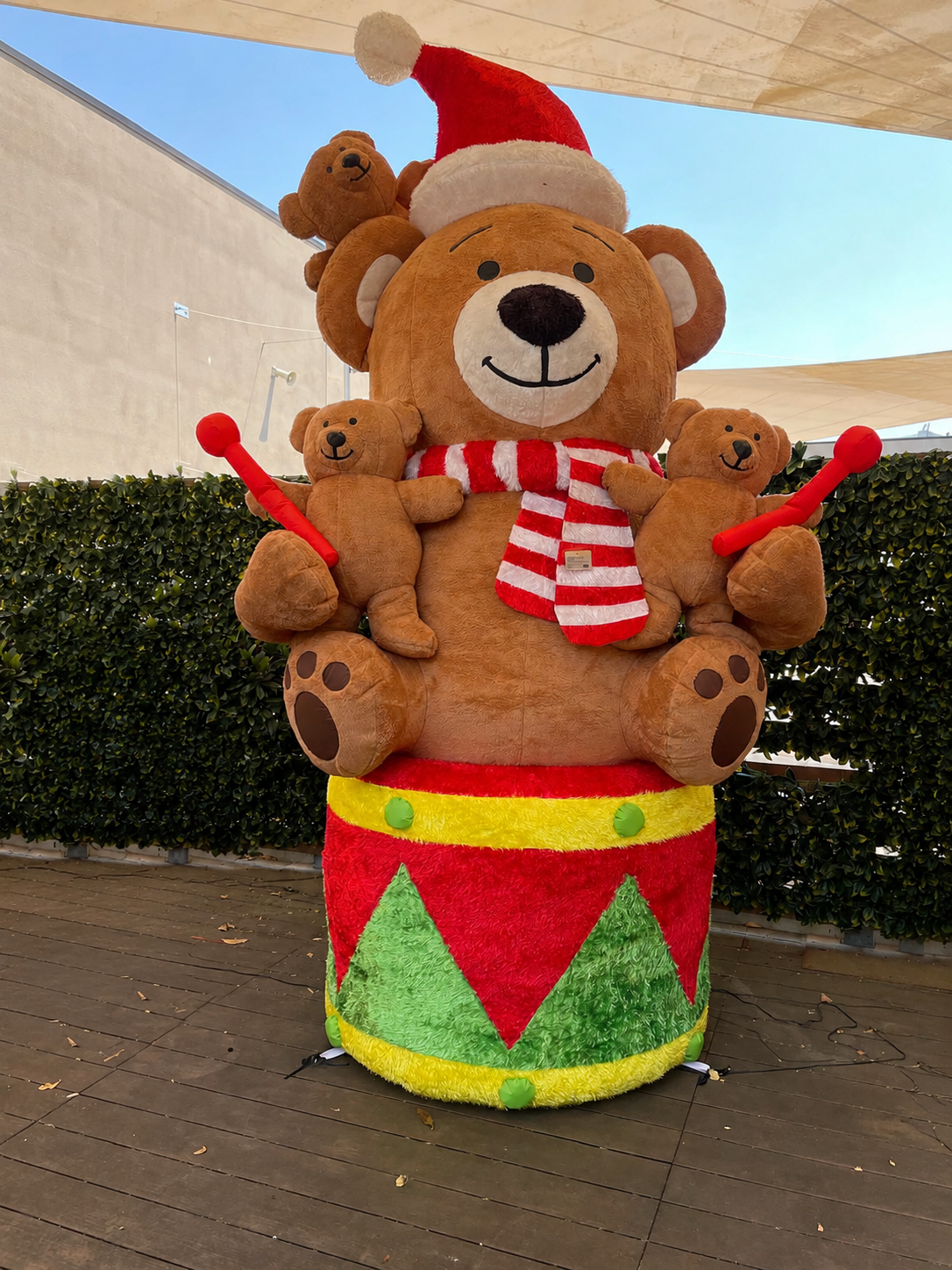 Maxi orso gonfiabile natalizio da esterno EDG alto 280 cm, seduto su un tamburo festivo con orsetti piccoli, sciarpa a righe e cappello di Babbo Natale su sfondo chiaro.