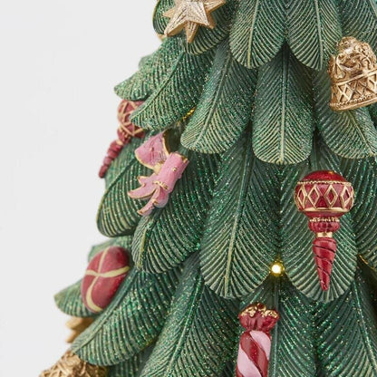 Dettaglio ravvicinato delle decorazioni dell'albero in poliresina EDG: aghi di pino con glitter verde, fiocco rosa, campanella dorata e dolciumi dipinti a mano.