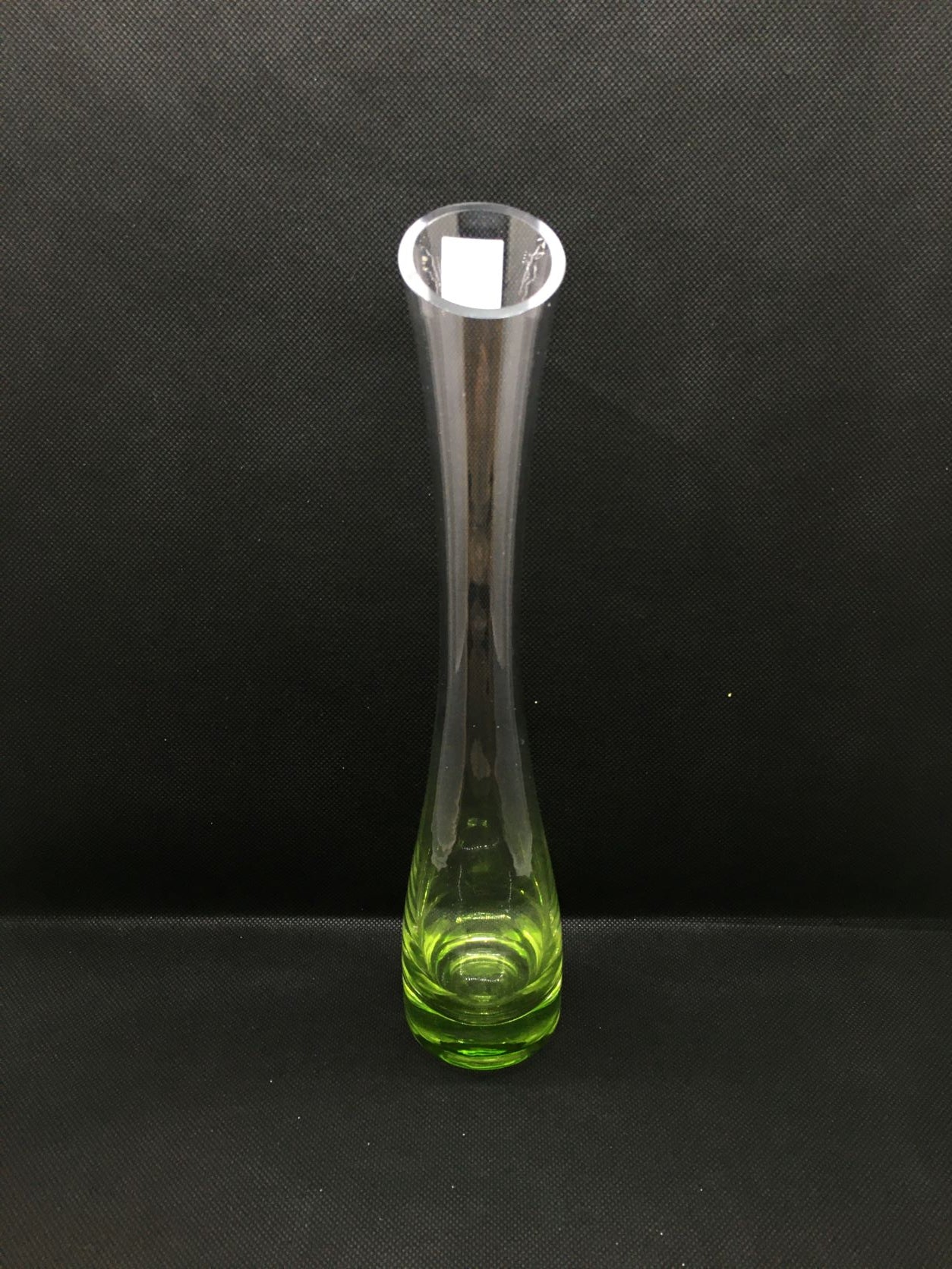 Vasetto monofiore in vetro trasparente con base di colore verde, collo stretto e apertura allargata con taglio obliquo.  Dimensioni: h 27 x 5 cm